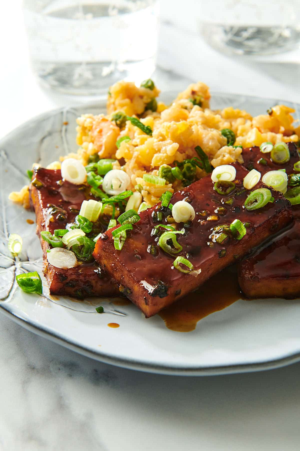 Tofu cooked in Asian BBQ sauce on plate with chopped scallions and rice.