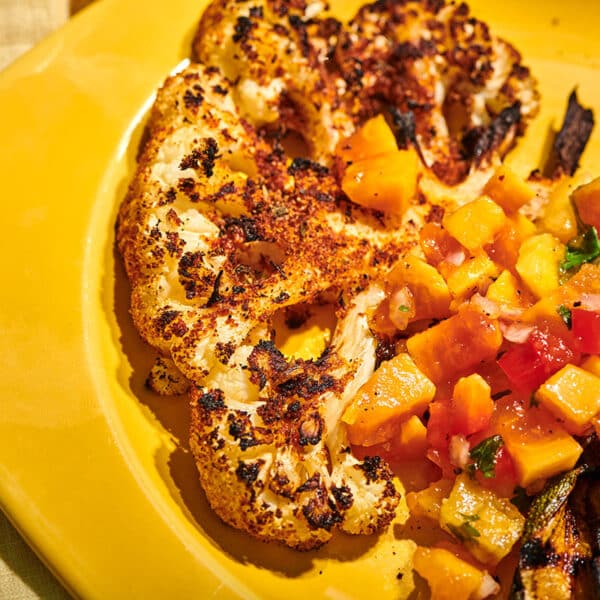 Grilled blackened cauliflower steak on yellow plate with salsa.
