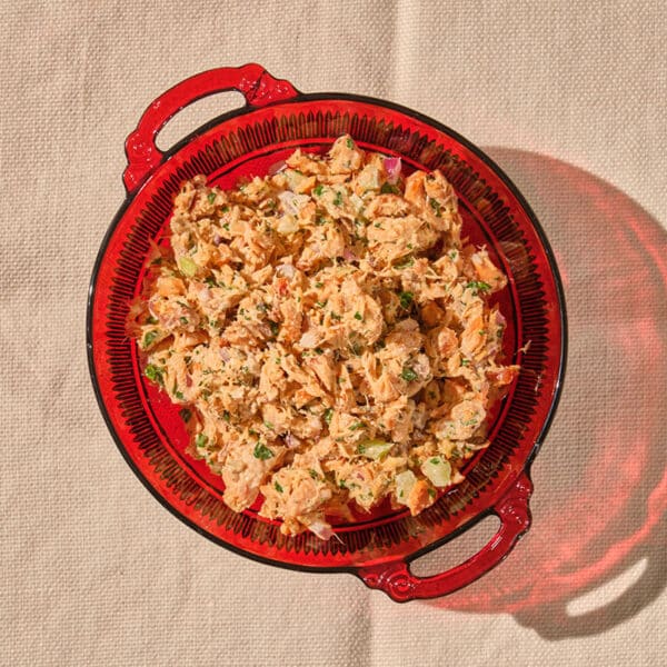 Canned salmon salad in red glass bowl on table.