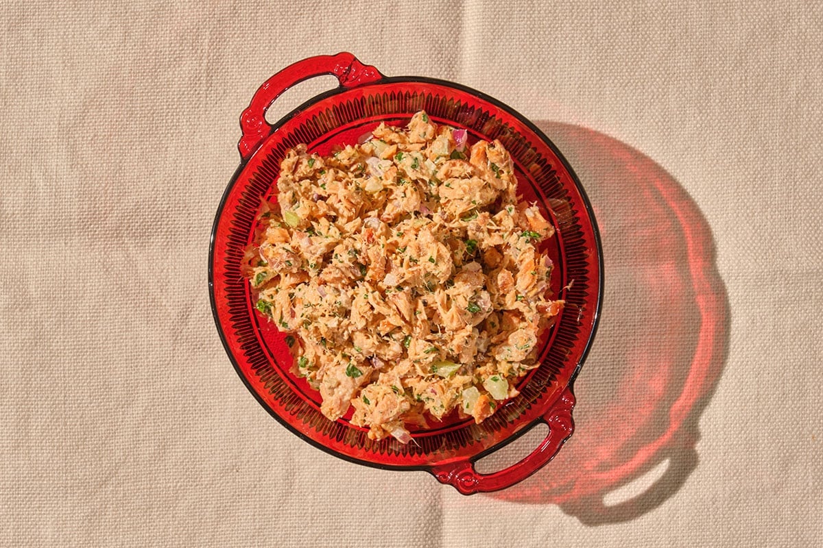 Canned salmon salad in red glass bowl on table.