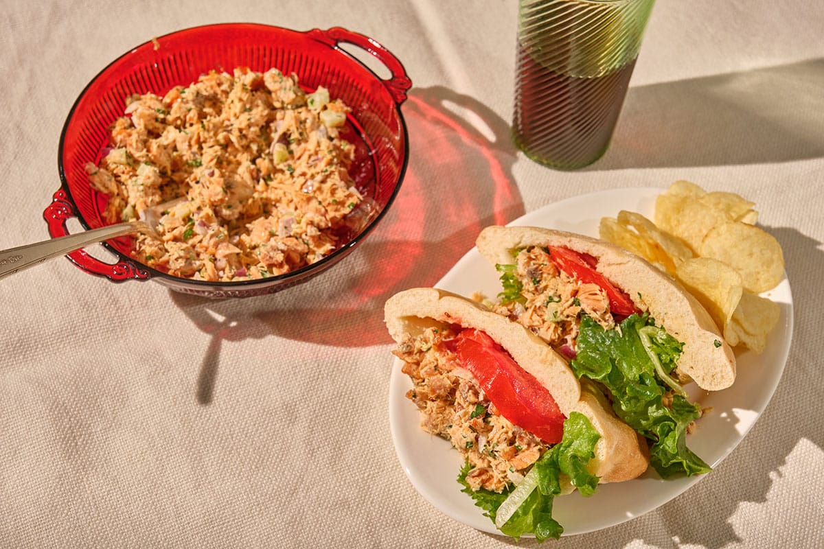 Salmon salad in red bowl and used in sandwiches with tomato and lettuce.
