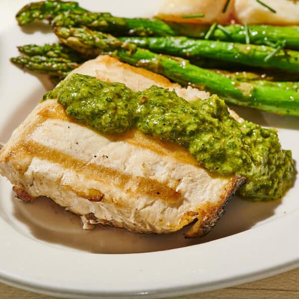 Grilled halibut with persillade sauce on plate with asparagus.