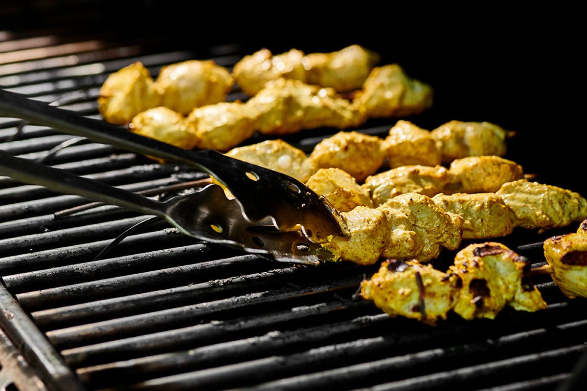 Grilling skewered tandoori marinated chicken and flipping with tongs.