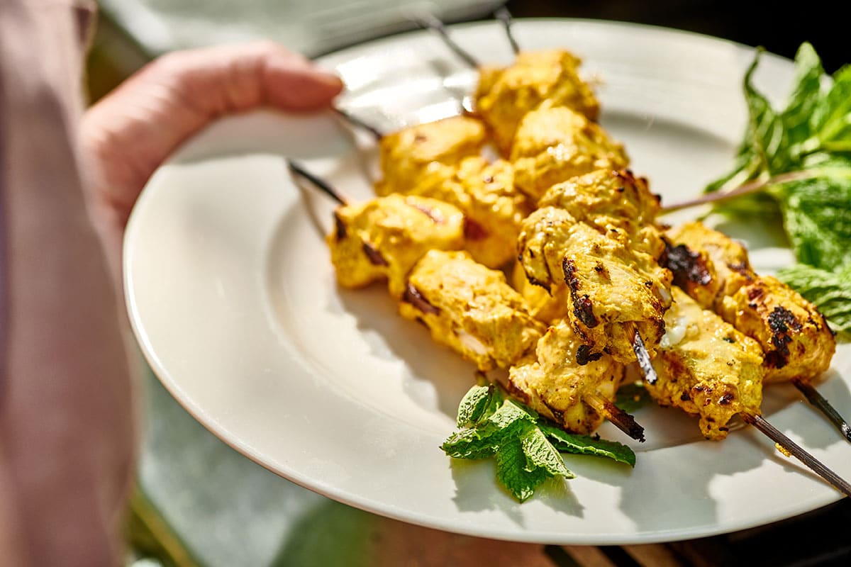 Woman serving tandoori chicken kabobs on plate with mint and rice.