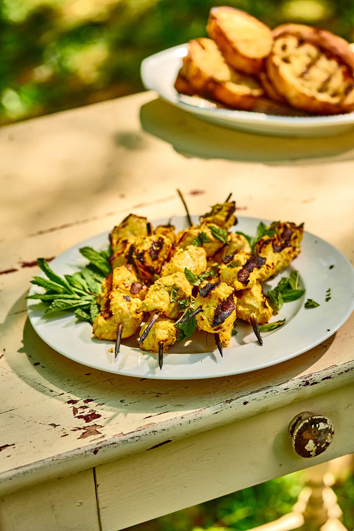 Skewered tandoori chicken kebabs on plate with mint at picnic.