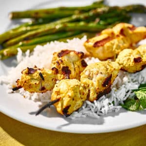 Grilled tandoori chicken skewered on plate with asparagus and other sides.
