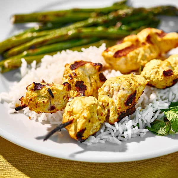 Grilled tandoori chicken skewered on plate with asparagus and other sides.