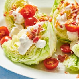 Classic wedge salad with tomatoes, bacon, cheese, and dressing on plate.