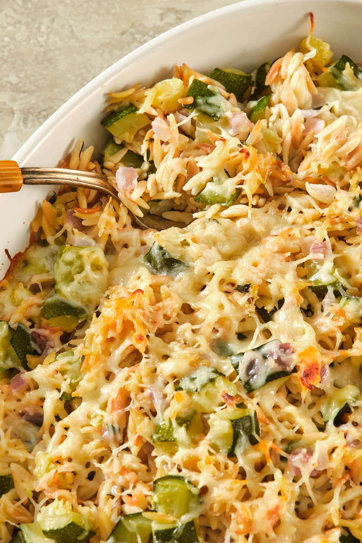 Woman using spoon to serve baked zucchini and orzo casserole from dish.