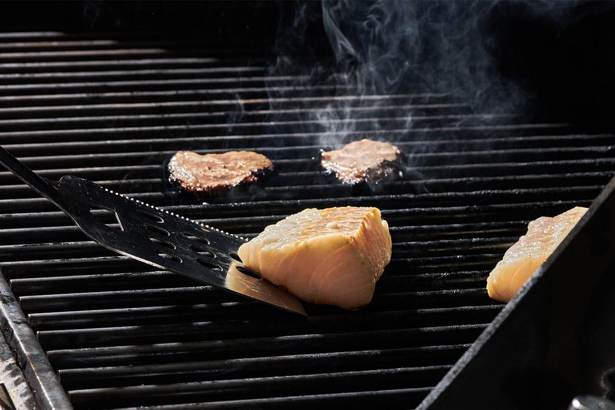 Flipping cod filets on grill with spatula.