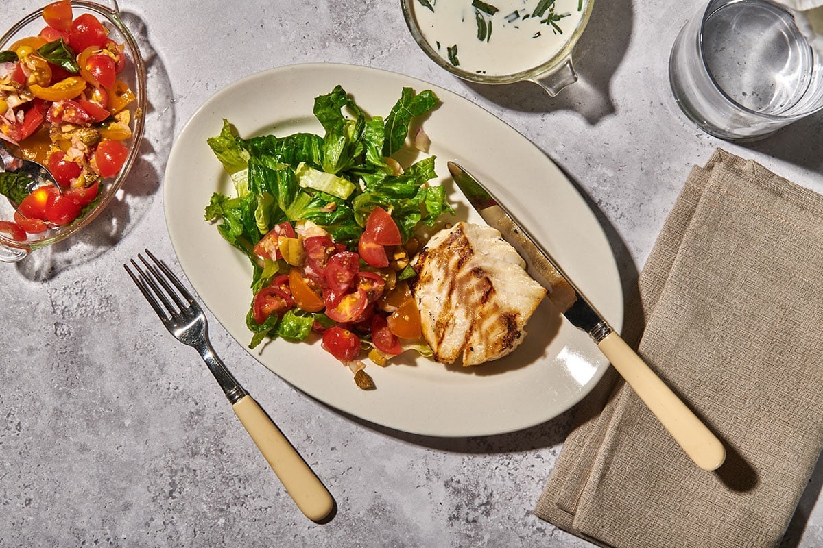 Grilled cod on plate with side salads and silverware.
