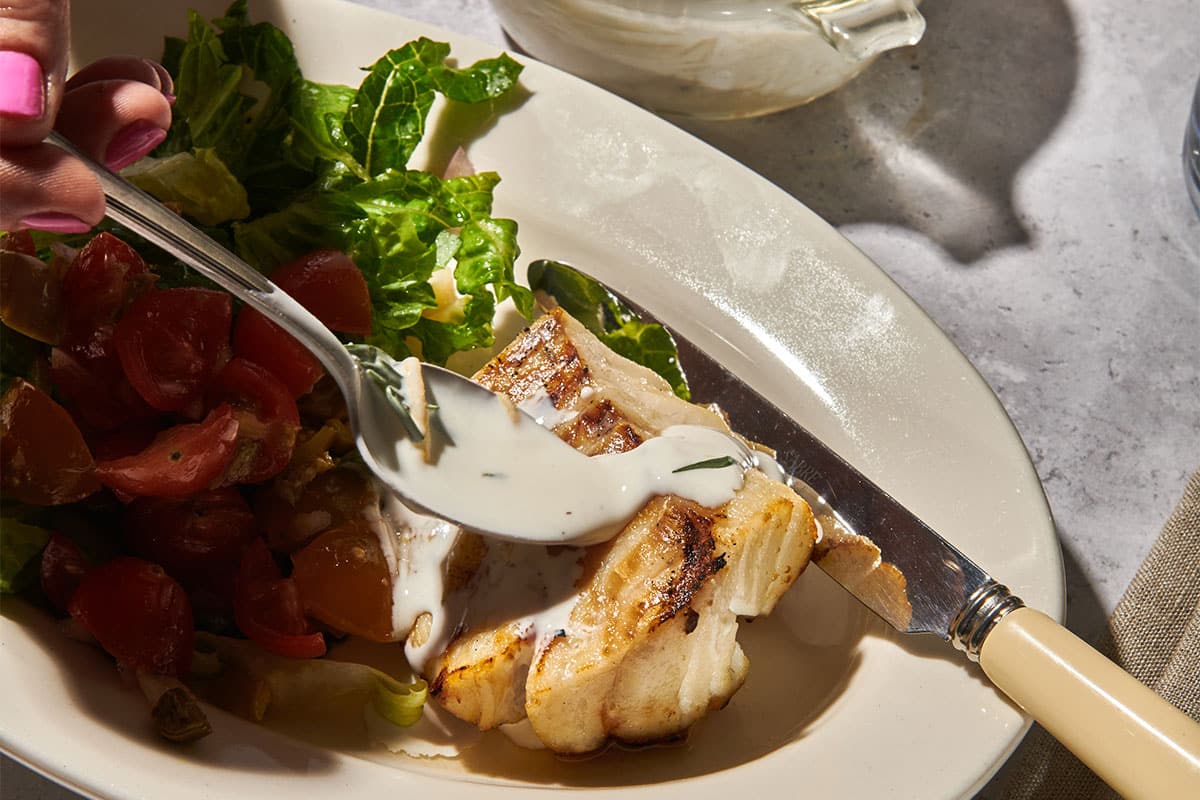 Topping grilled cod with lemon sauce on plate.