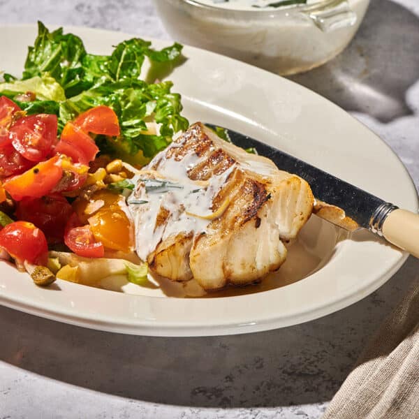 Grilled cod filet with lemon sauce on plate with salads.