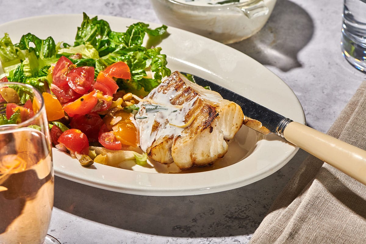 Grilled cod filet with lemon sauce on plate with salads.
