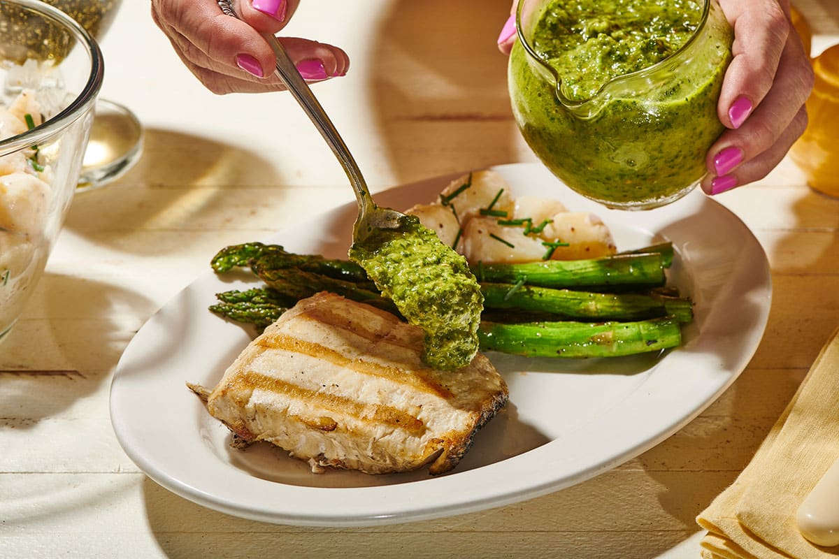Woman spreading persillade sauce over grilled halibut on plate.