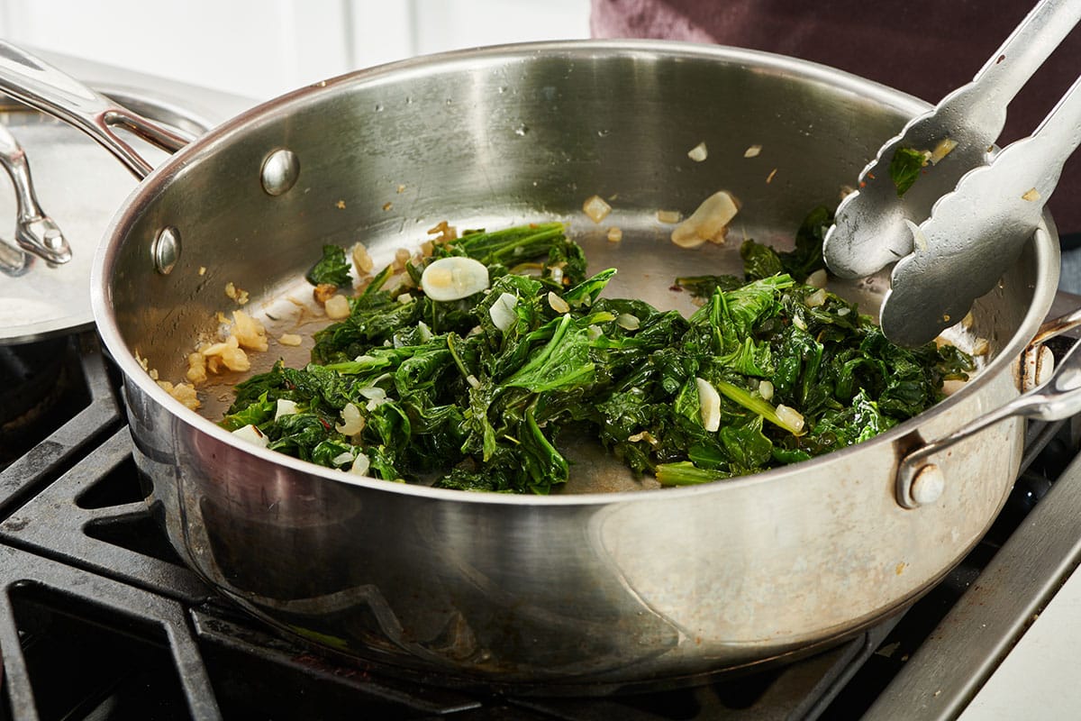 Sautéing mustard greens with onions and garlic in pan.
