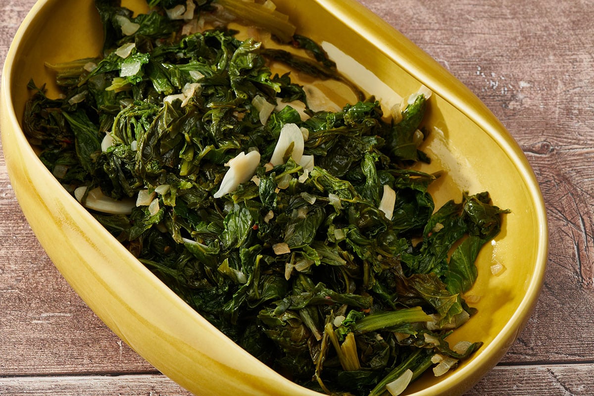 Sauteed mustard greens in yellow serving dish on table.