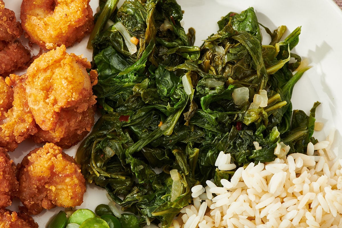Cooked mustard greens on plate with rice and hush puppies.