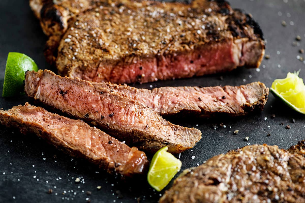 Grilled Mexican Rib-Eye Steaks sliced on cutting board with limes