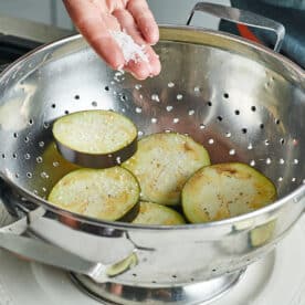 Adding salt to eggplant slices in colander.