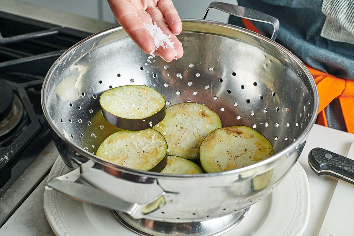 Adding salt to eggplant slices in colander.