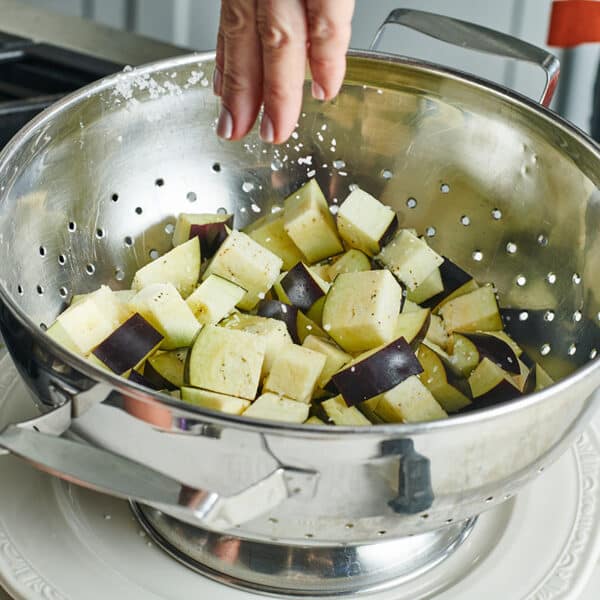 Adding salt to cubed eggplant in metal colander.