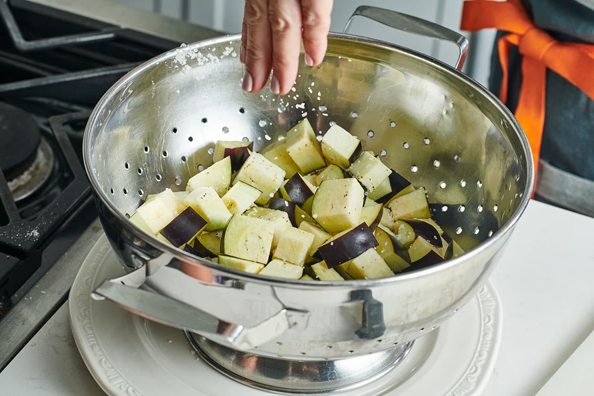 Adding salt to cubed eggplant in metal colander.
