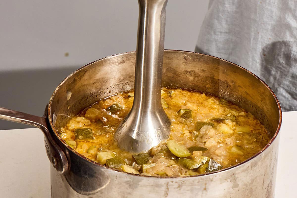 Pureeing zucchini soup in pot with immersion blender.