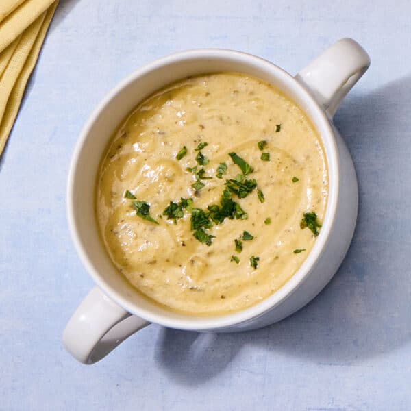 Bowl of zucchini cheddar soup on blue table.