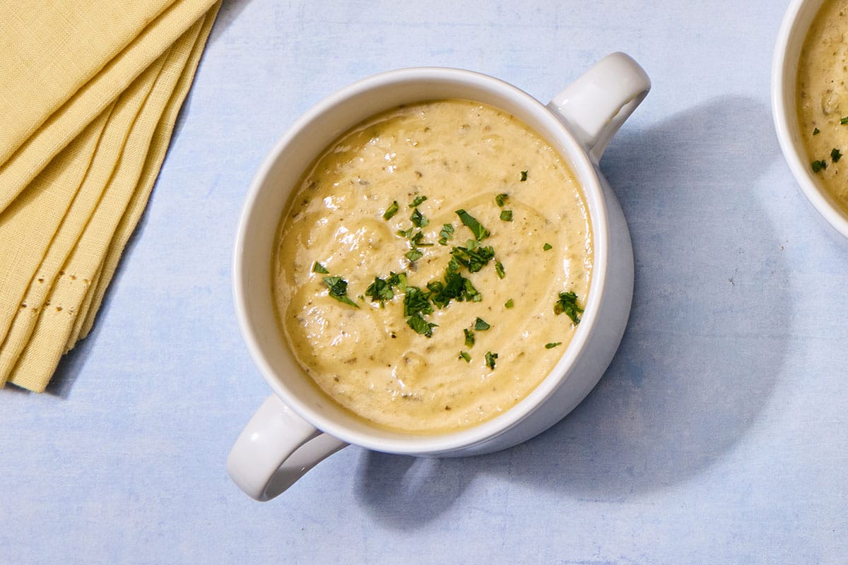 Bowl of zucchini cheddar soup on blue table.