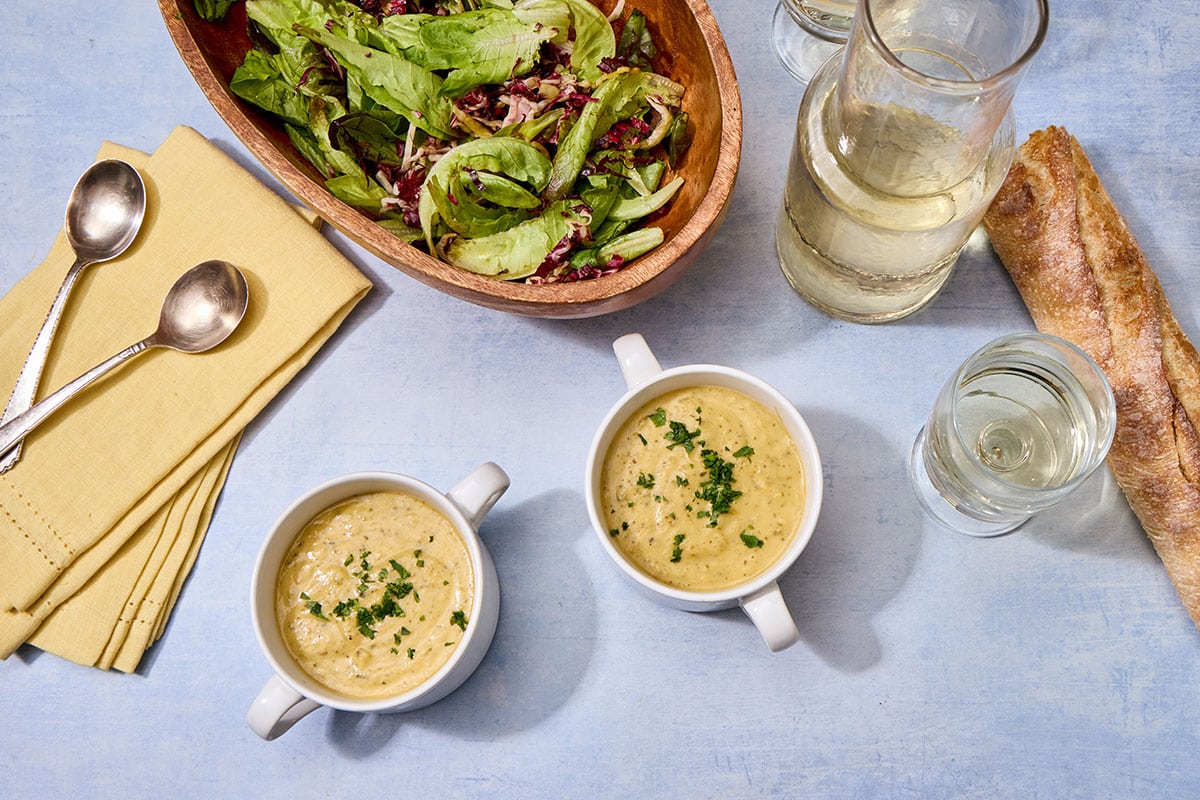 Zucchini cheddar soup in two bowls on table with salad, drinks, and silverware.