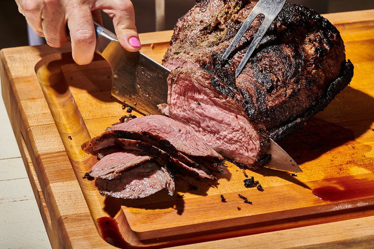 Woman slicing Santa Maria style grilled tri-tip steak with large knife.