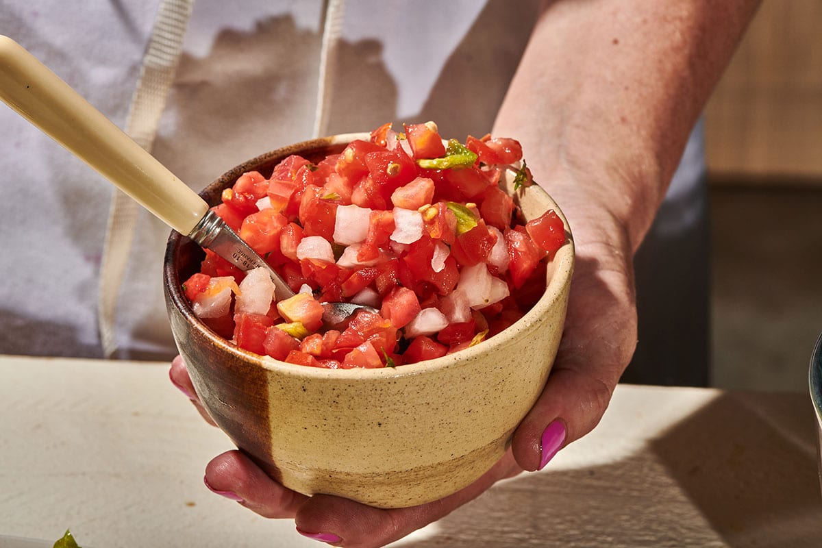 Woman holding small bowl of pico de gallo.