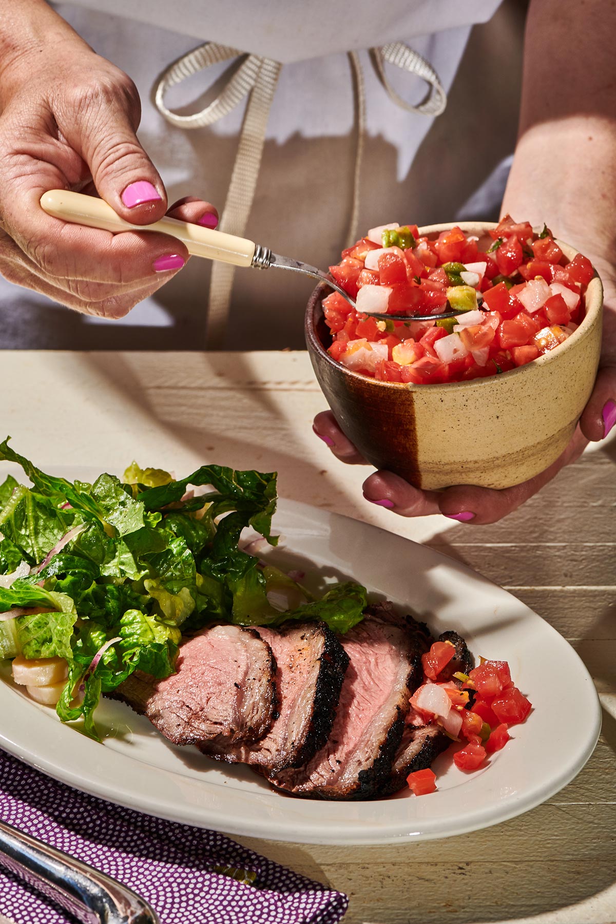 Woman adding pico de gallo to plate with sliced Santa Maria tri-tip.