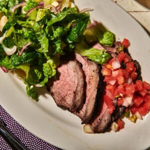 Sliced Santa Maria grilled tri-tip steak on plate with salsa and salad.