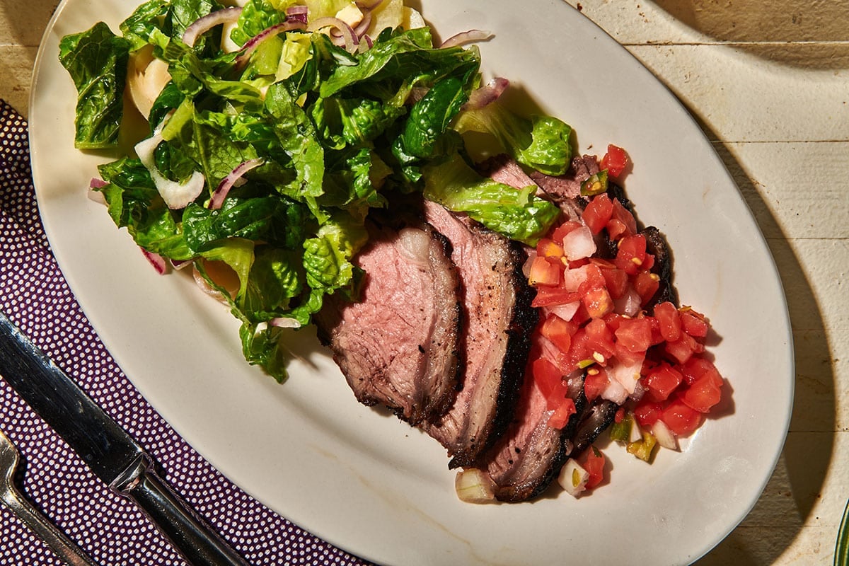Sliced Santa Maria grilled tri-tip steak on plate with salsa and salad.
