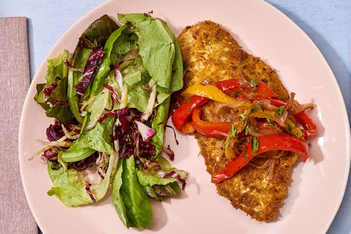 Breaded chicken cutlet on pink plate with pepperonata and salad.