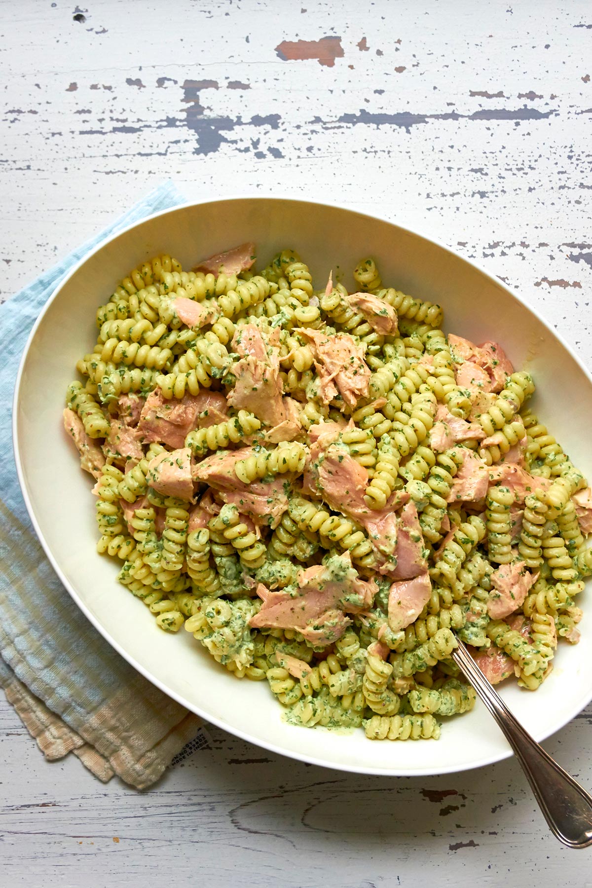 Pasta salmon salad in bowl on white wood table.