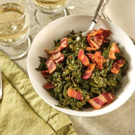 Southern mustard greens in bowl on table with bacon on top.