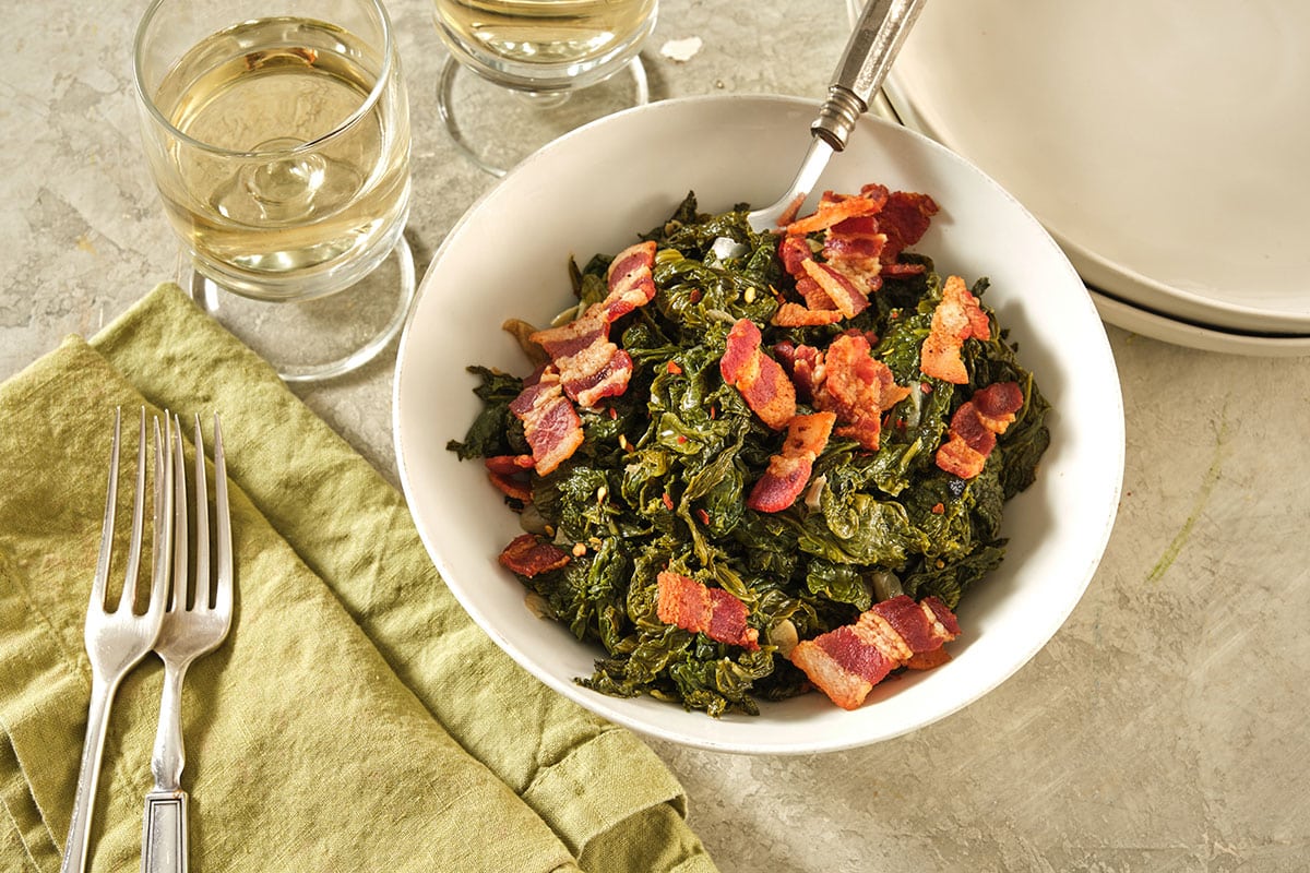 Southern mustard greens in bowl on table with bacon on top.