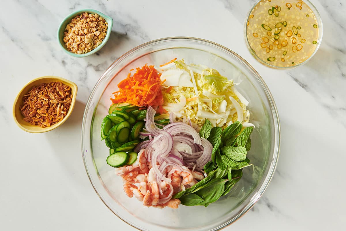 Bowls with Vietnamese dressing, chopped salad ingredients, fried shallots, and roasted peanuts on table.
