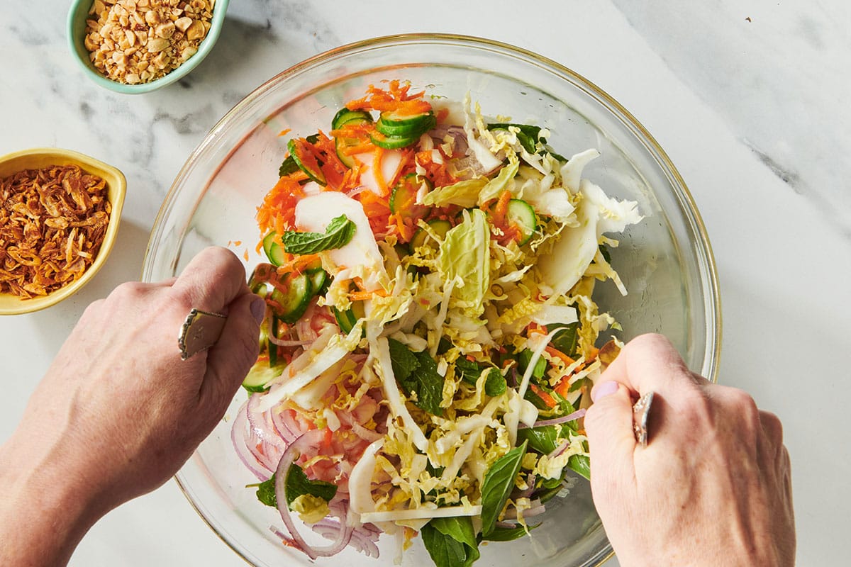 Woman tossing cabbage salad with Vietnamese dressing in glass bowl.