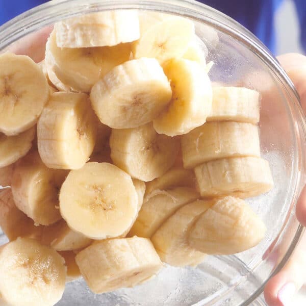 Woman pouring sliced bananas out of glass bowl.