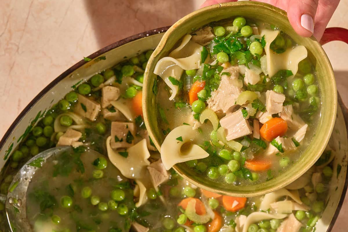 Serving turkey soup with peas and noodles in bowl.