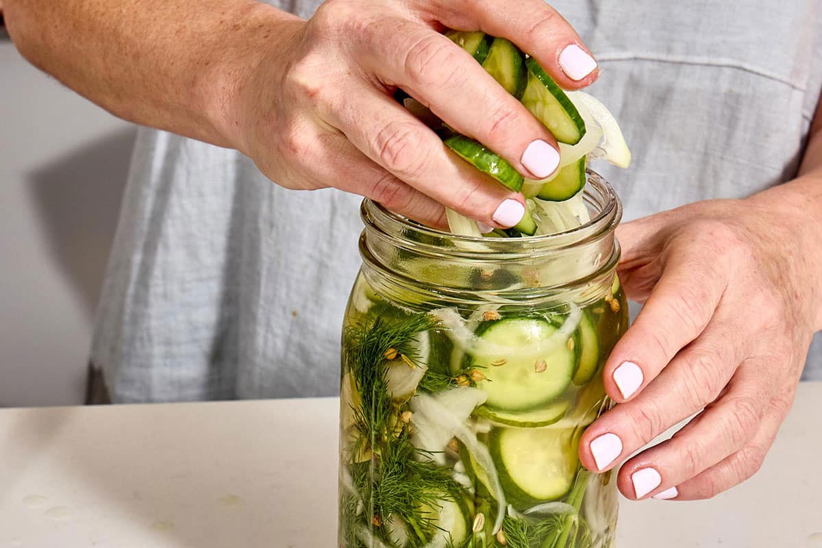 Packing sliced cucumbers, dill, and brine into glass Mason jar.