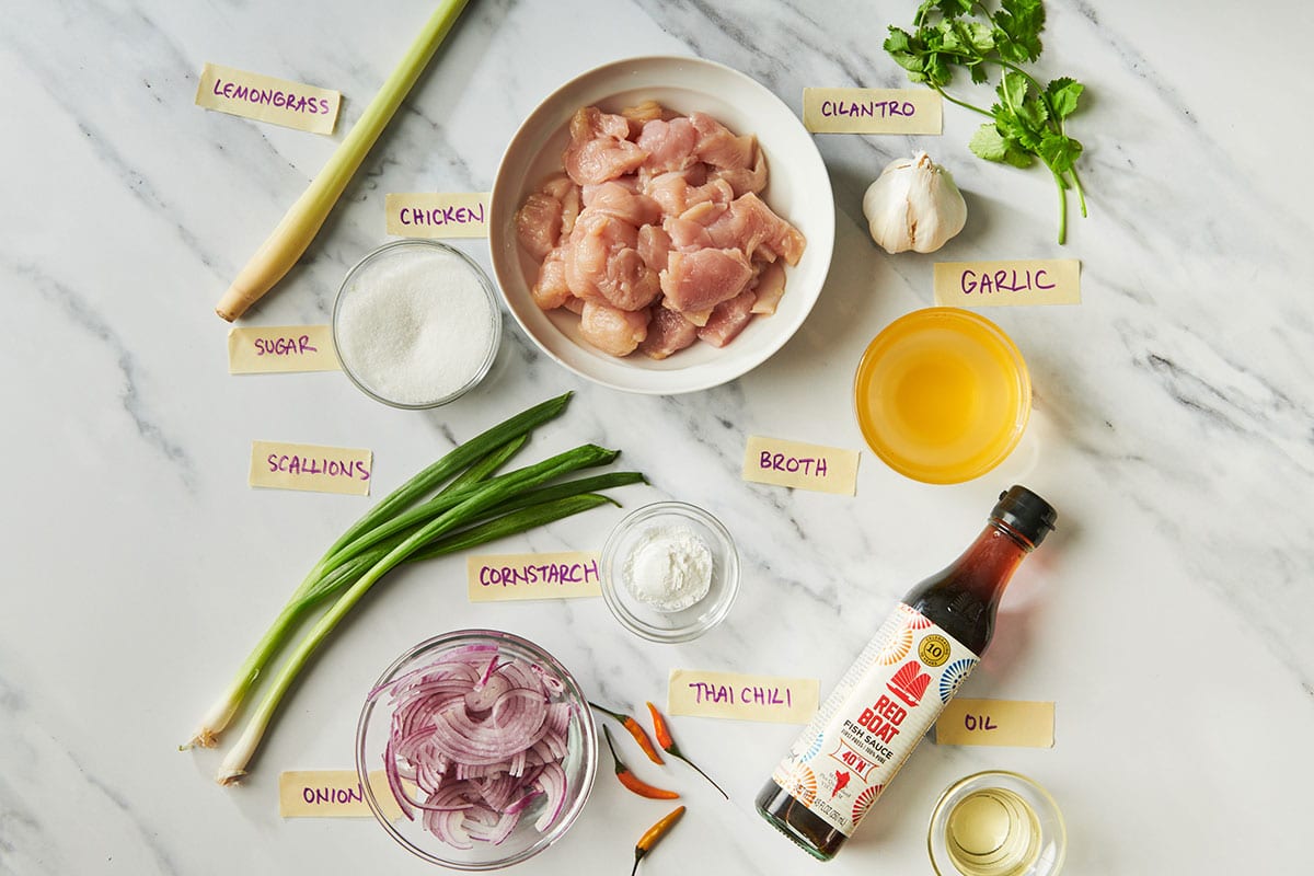 Lemongrass, chicken, and other stir-fry ingredients on white marble table.