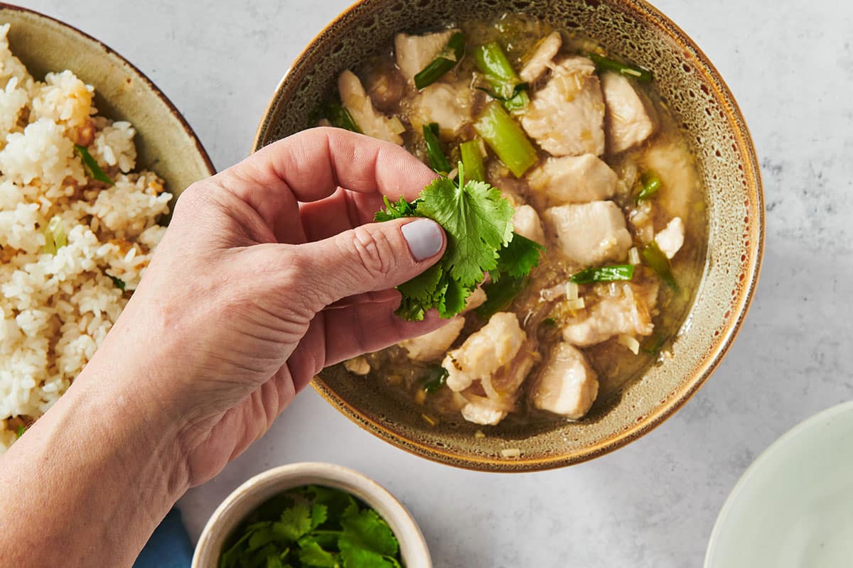 Adding fresh cilantro on top of stir-fried chicken and lemongrass in bowl.