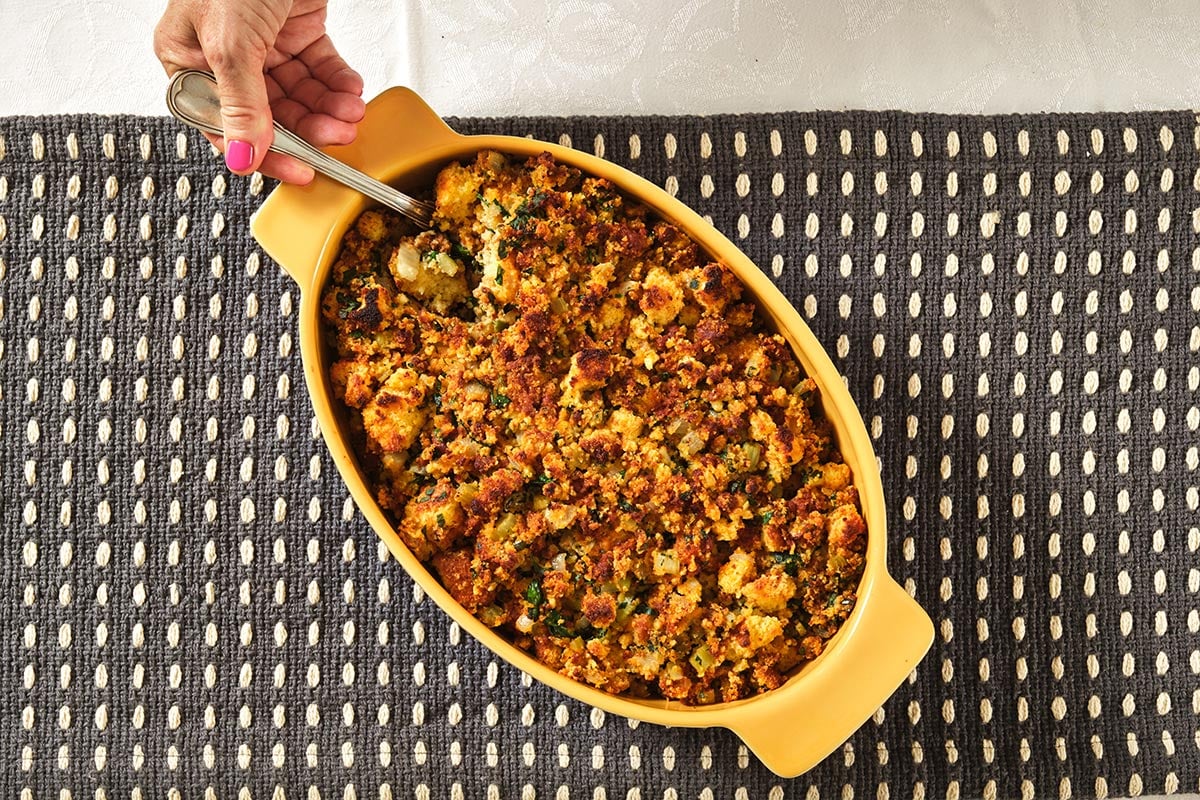 Serving chorizo and cornbread stuffing with spoon from yellow dish.