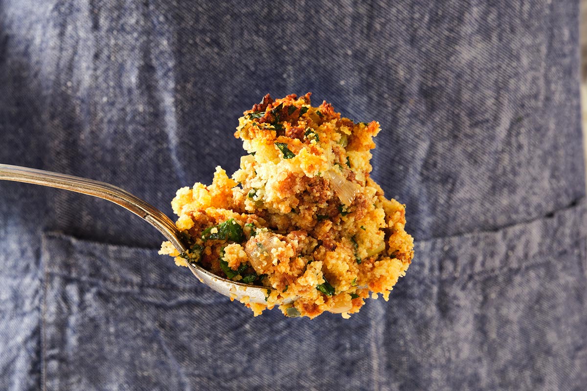 Woman holding spoonful of chorizo cornbread dressing.