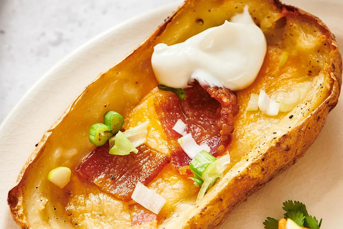 Loaded baked potato skin on plate with cheese, bacon, chives, and sour cream.